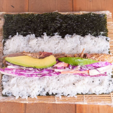 A sushi mat topped with pulled pork sushi ingredents ready to be rolled.