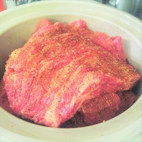 Slow cooker bowl with raw seasoned brisket sitting in it.