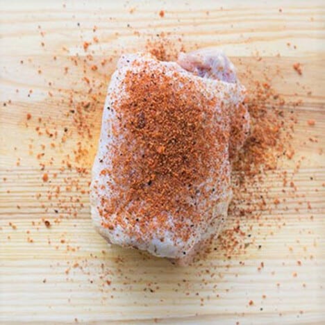 Looking down on a well trimmed chicken thigh sprinkled with a rub.