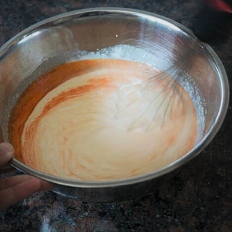 A stainless bowl with predominatly white and orange ingredients being mixed together.