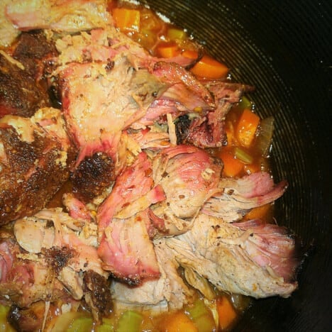 Looking down into a saute pan of shredded lamb, carrots, celery, and onions.