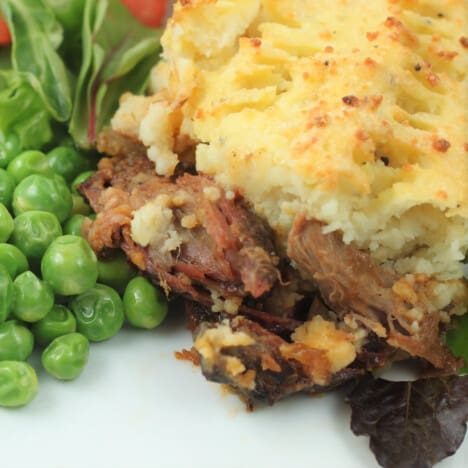 A scoop of shepherds pie with shredded lamb and green peas on a white plate.