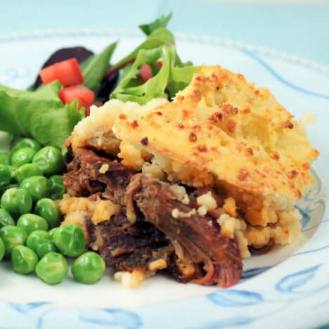 A blue and white plate with a scoop of shepherds pie and green peas.