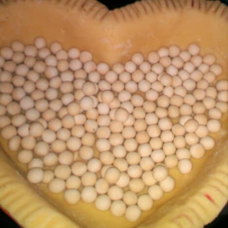 A heart shaped raw pie crust wit a layer of pie beads.