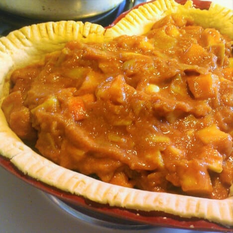 A heart shaped red pie dish with a pie crust with an apple filling in it.