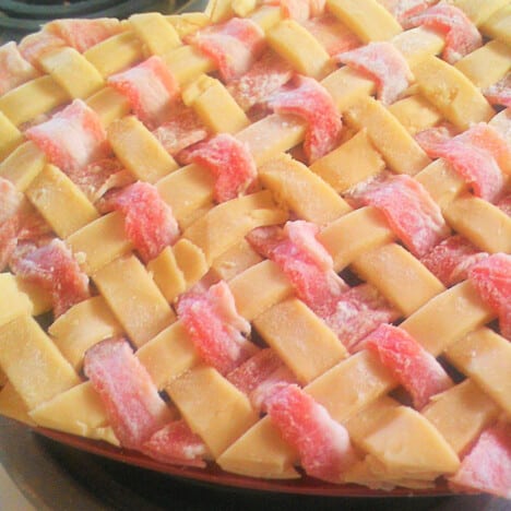 Close up of a raw apple and bacon lattice sitting ontop of a pie.