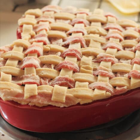 A bacon and pastry lattice in a red baking dish trimmed and ready to bake.,