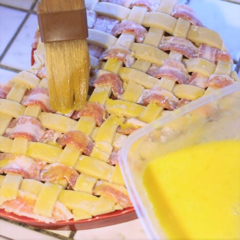 A partyry brush adding an egg yolk wash to the top of a bacon and pastry lattice.