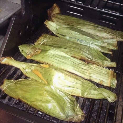 Banana leaf bundles are laid across a hot grill.