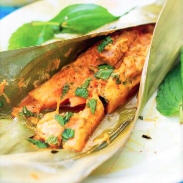 A cooked piece of marinated salmon is peeking out of a piece of banana leaf.