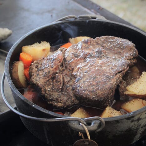 A Dutch oven with its lid off showing a steaming pot roast with vegetables.