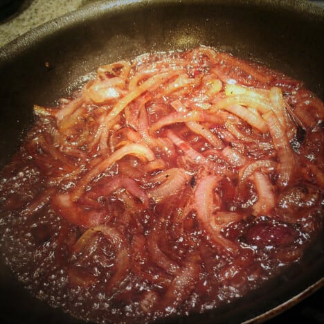 Sliced red onions are simmering in a skillet with red wine.