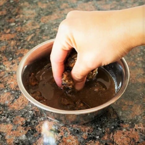 A hand is mixing a small bowl of tamarind paste with hot water.