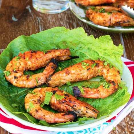 Three grilled prawns, heads on, rest on a piece of lettuce.