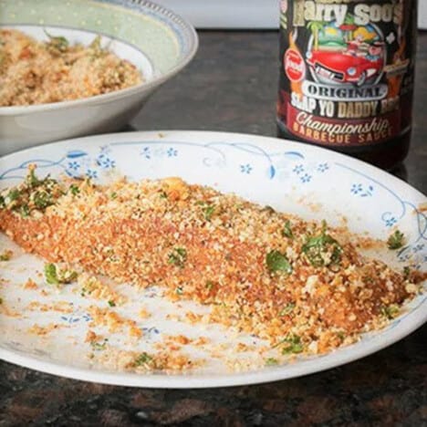 A cracker crumbed piece of salmon ready to be cooked sitting on a plate.