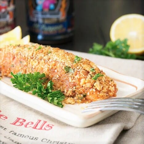 A baked cracker crumbed salmon fillet served on a white plate.