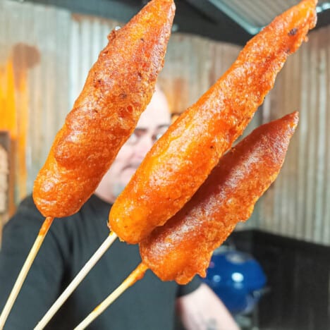 Three deep fried carrots being held up on their skewers.