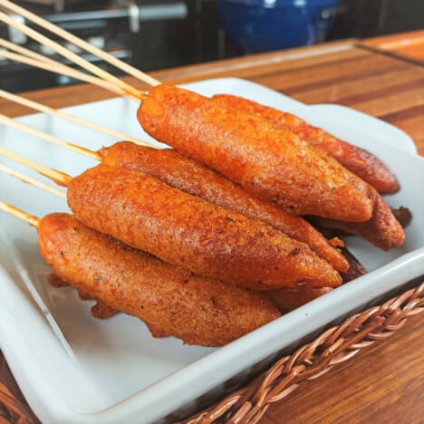 Square white plate serving skewered deep fried carrots.