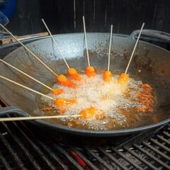 A cast iron wok over fire cooking skewered carrots.