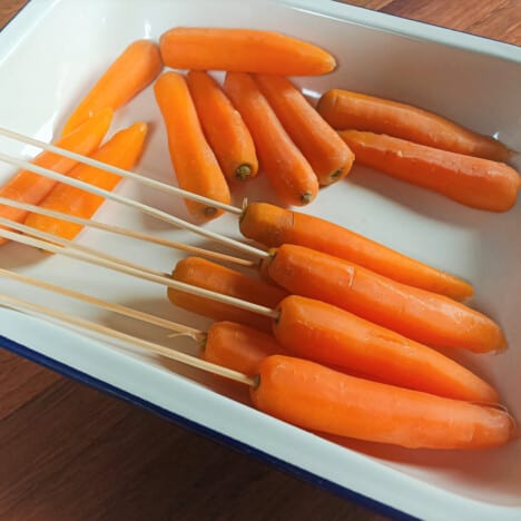 White dish with carrots, some that have been skewered.