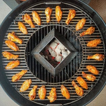 Looking directly down over a kettle grill with a circle of chicken wings and a kettle kone of charcoal in the middle.