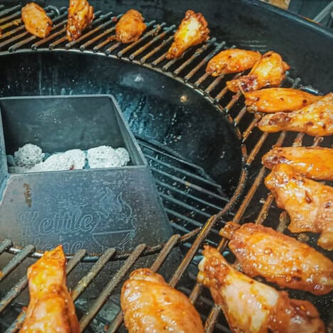Chicken wings cooking on a kettle grill with the heat kept in the center.