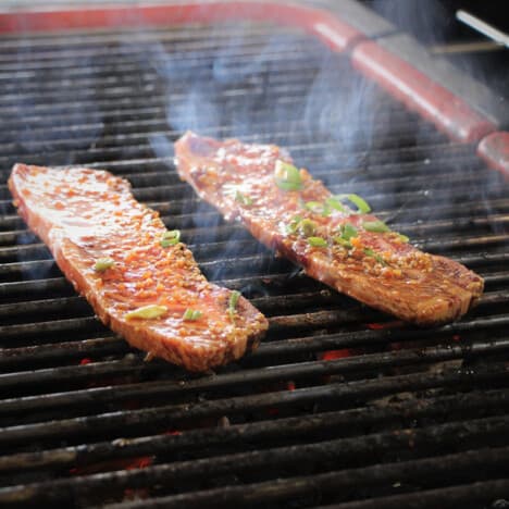 Two thin cut short ribs grilling on the barbecue.