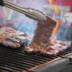 A beef short rib on a grill being turned with tongs.