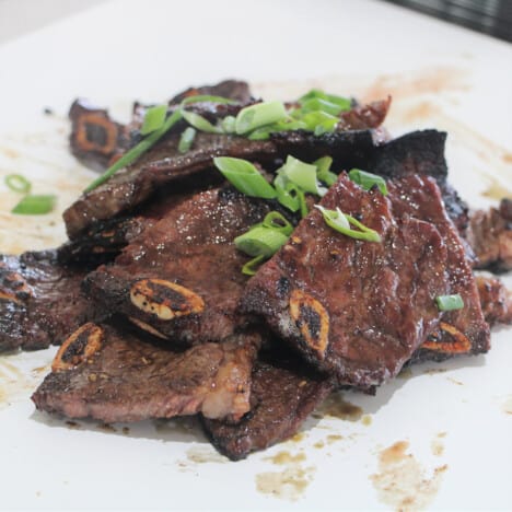 A pile of kalbi grilled beef short ribs garnished with sliced green onions.