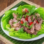 Slices of cooked rib-eye on a plate of lettuce, garnished with red pepper slices.
