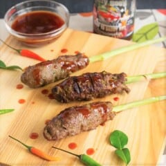 Three cooked lemongrass beef skewers are drizzled with barbecue sauce and laying on a wood cutting board.