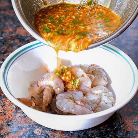 A bowl of marinade is being poured over raw shrimp.