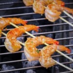Four shrimp are skewered on to bamboo skewers on the grill.