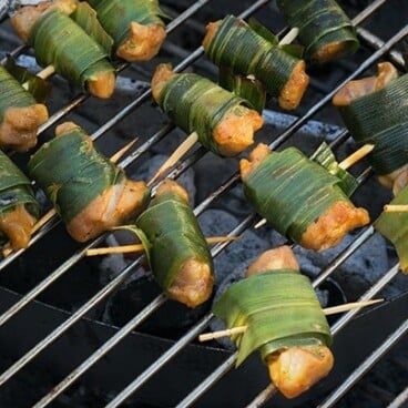 Individually wrapped pandan and chicken pieces on a hot grill.