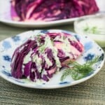 A plate with a wedge serving of purple cabbage topped with a yogurt sauce and fresh dill.