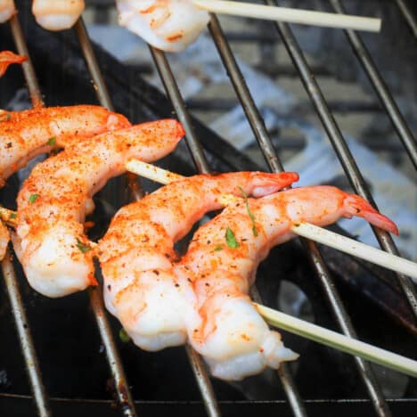 Three cooked and seasoned shrimp skewered on two skewers laying across grill grates.