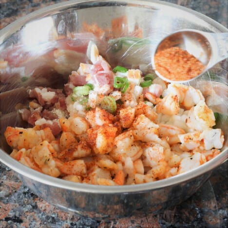 A stainless steel mixing bowl with chopped shrimp, bacon, cream cheese, and seasoning.