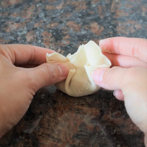 A pair of hands folding a wonton on a marble countertop.