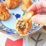 A hand holds up a fried wonton missing a bite, revealing the filling.