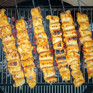 Six calamari skewers are cooking over a charcoal grill.