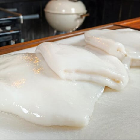Cleaned calamari (squid hoods) sitting on a chopping board.