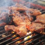 Chicken thighs grilling over charcoal.