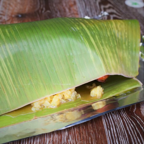 A large banana leaf is folded over, with a bit of crushed pineapple spilling out.