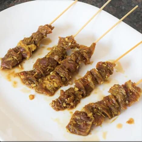 Raw satay skewers sit on a white plate.
