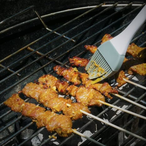 Beef satay skewers are on the grill being basted with the marinade.