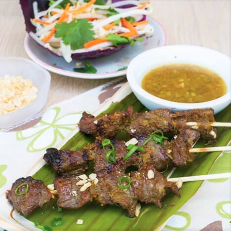 Grilled skewers are served on a banana leaf with dipping sauce and a vegetable slaw.