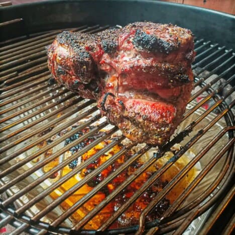 A boned lamb leg sitting in the center of a round grill above a drip pan.