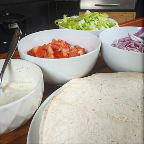 Pita bread on a plate with fillings of tomato, lettuce, red onion, and garlic yogurt sauce in the background.