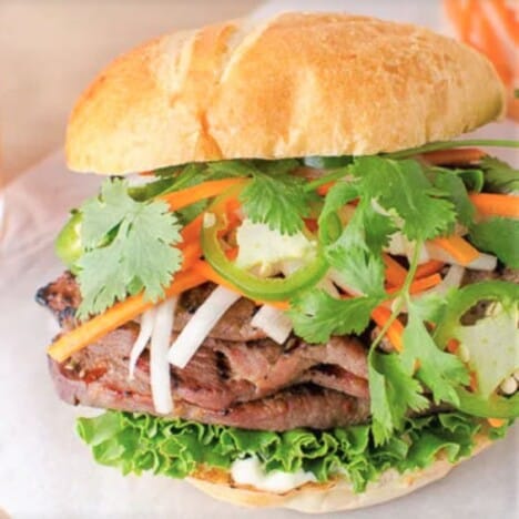 A slider bun with layers of lettuce, pork, carrot-daikon slaw, and fresh cilantro.