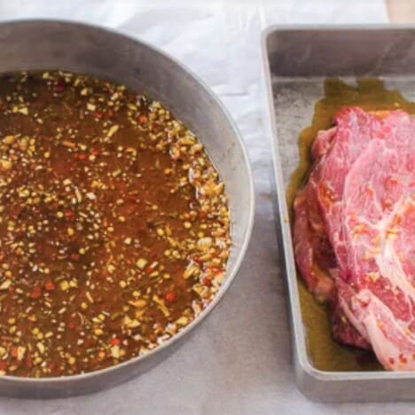 A bowl of marinade sits next to a tin container holding slices of raw pork.